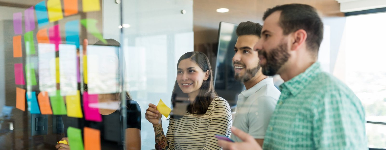 colegas-masculinos-femeninos-arreglando-notas-adhesivas-pared-vidrio-reunion-oficina-scaled-1.jpg